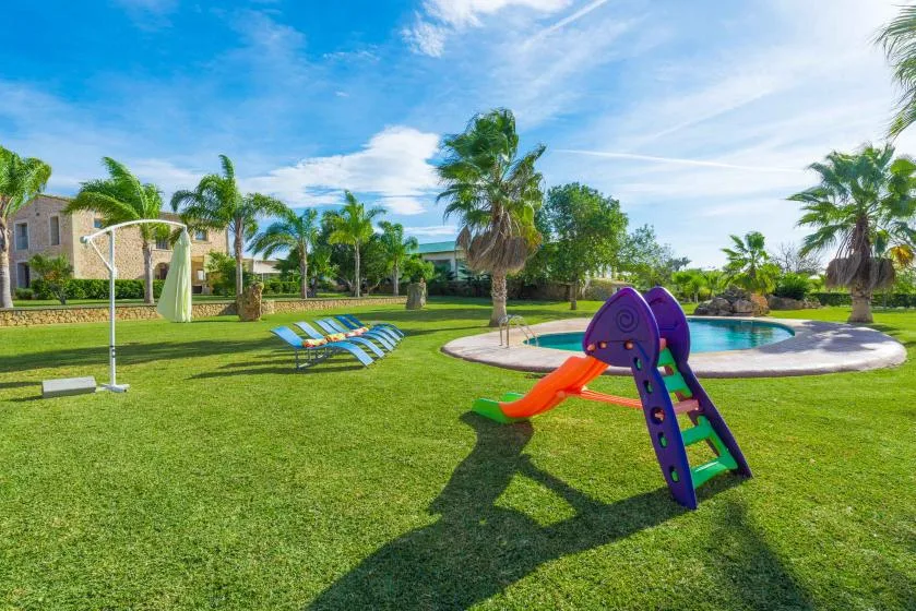 A grassy outdoor play area features a colorful slide beside a swimming pool.
