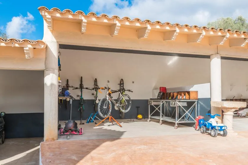 A covered outdoor storage area with bicycles, exercise equipment, and a child’s ride-on toy.