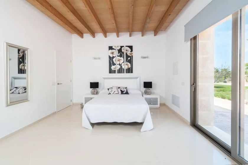 A bright bedroom with a bed beneath floral artwork and large sliding glass doors.