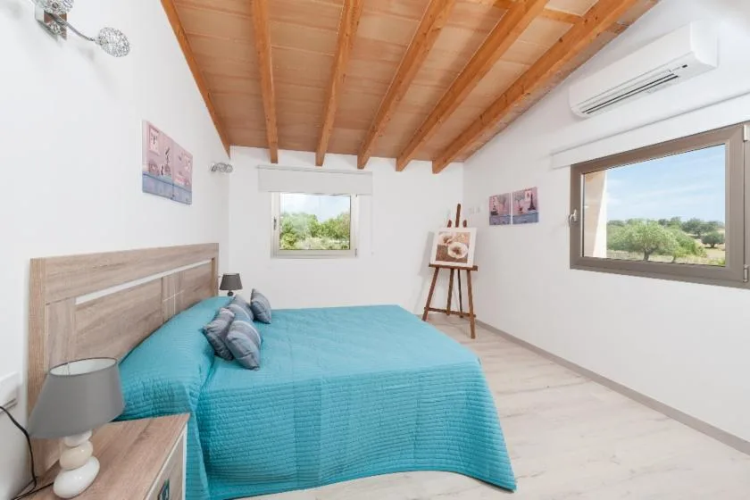 A bright bedroom with a turquoise bed and windows overlooking greenery.