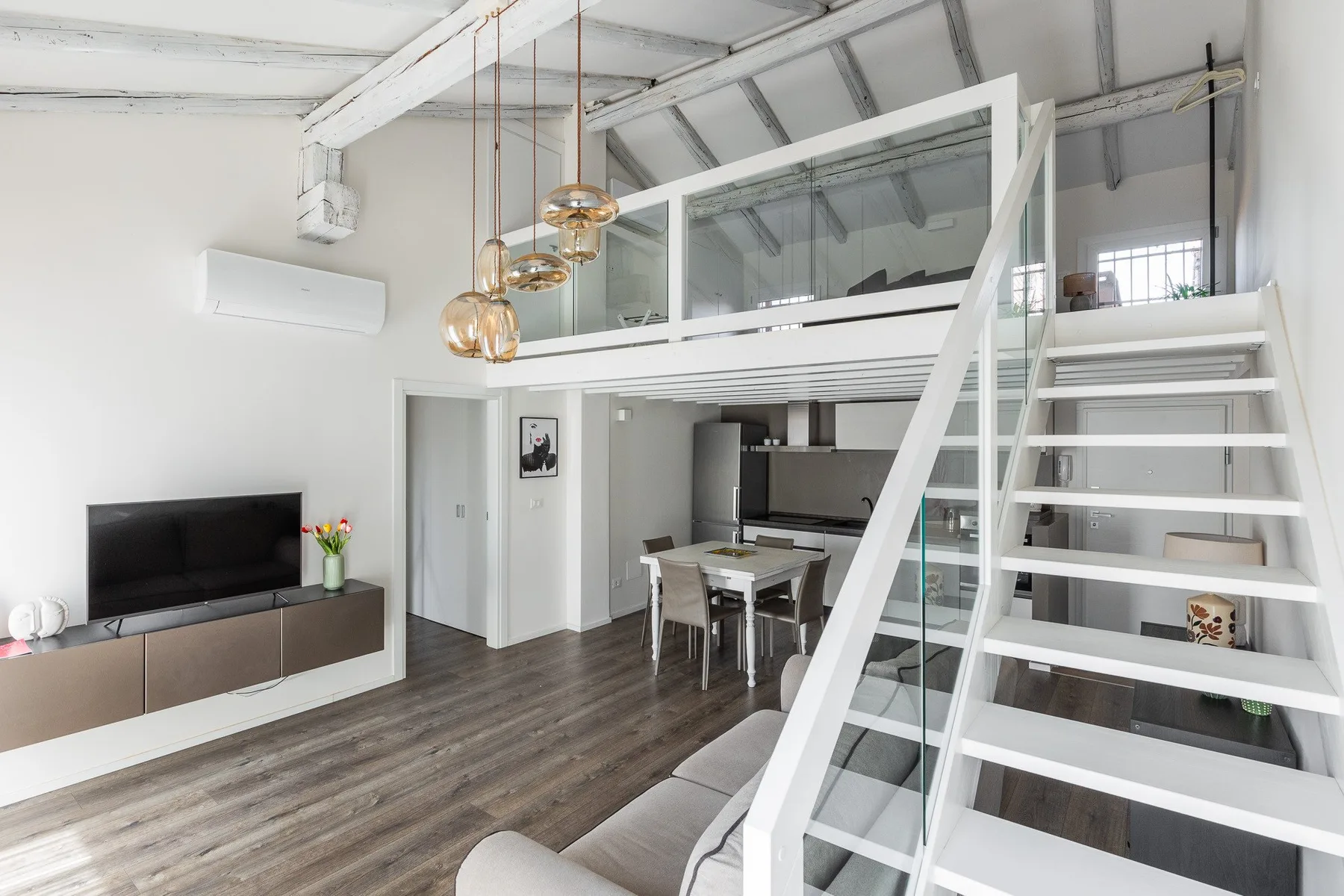 A bright open-plan living area has a dining table and stairs to a loft.