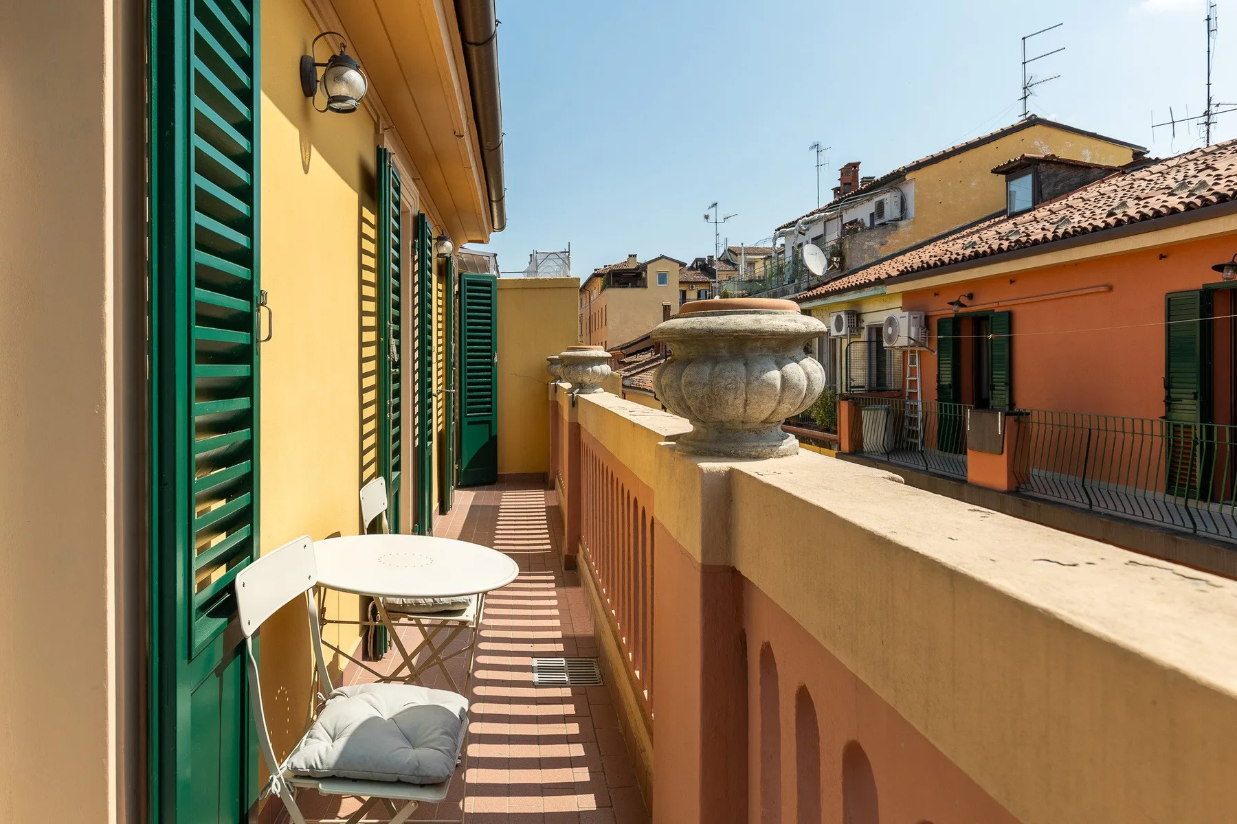 A narrow balcony with green shutters, a small table, and neighboring buildings.