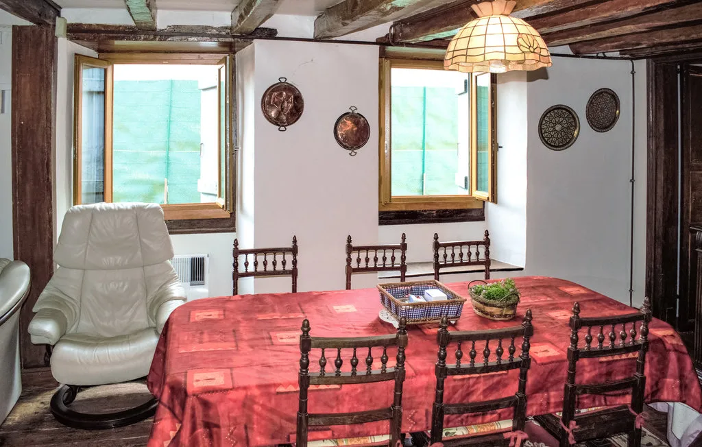 Un comedor con un mantel rojo, sillas de madera y ventanas luminosas.