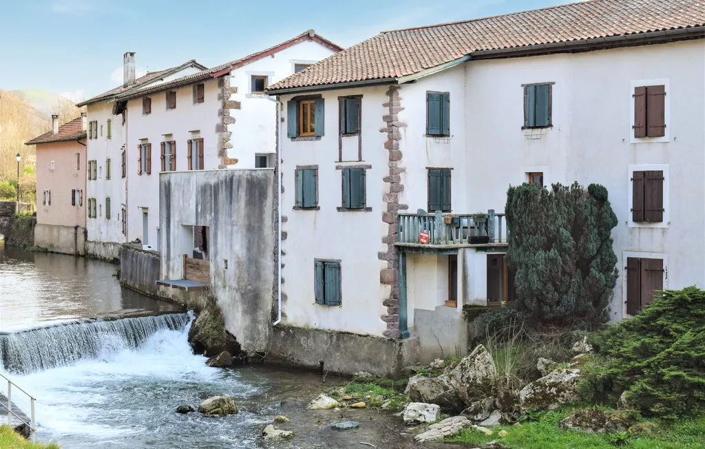 White buildings stand beside a flowing stream and small waterfall.