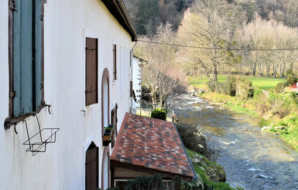 Un edificio junto al río, con techo de tejas, agua corriente y campos verdes.