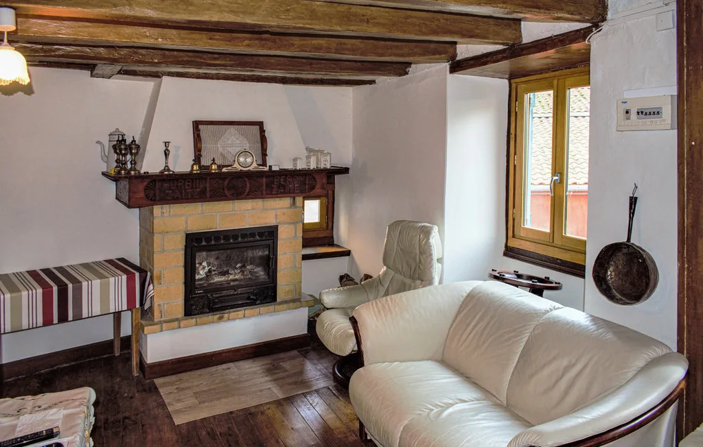A living room with a fireplace, pale seating, and exposed ceiling beams.