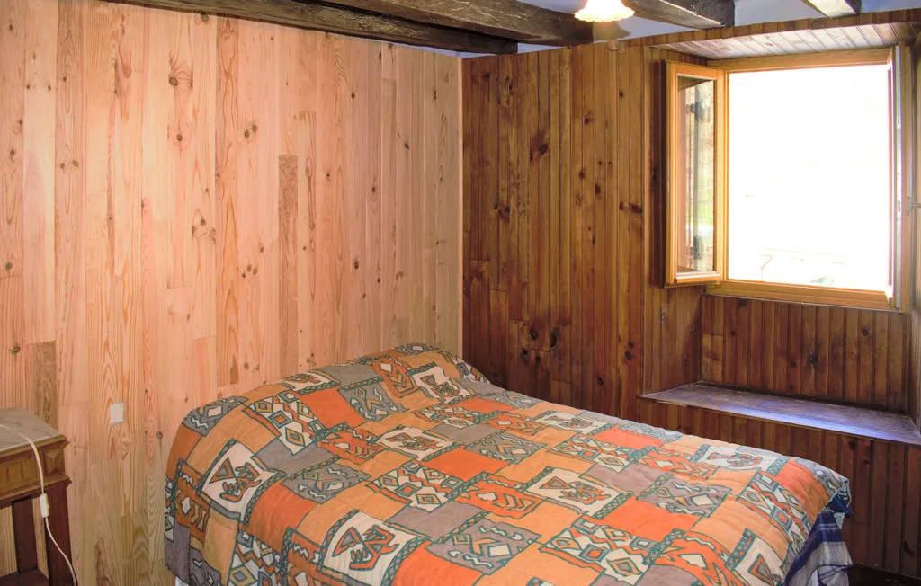 A bedroom with a bed covered by a patterned quilt beside a bright window.