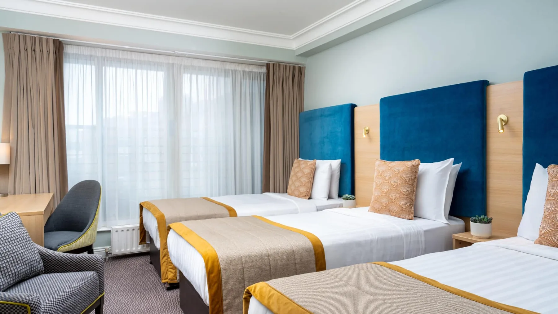 Triple room with three single beds, blue headboards and seating.