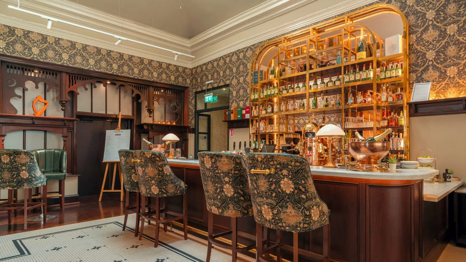 Hotel bar with ornate wallpaper, plush seating and backlit drinks display.