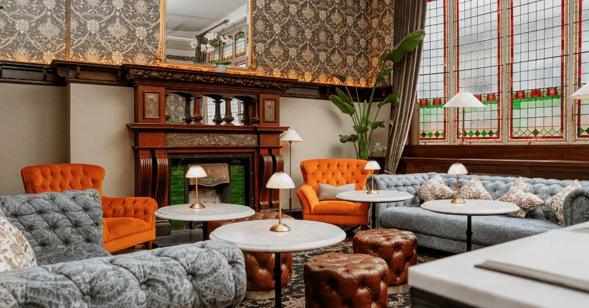 Hotel lounge with plush seating, marble tables, ornate fireplace and stained-glass windows.