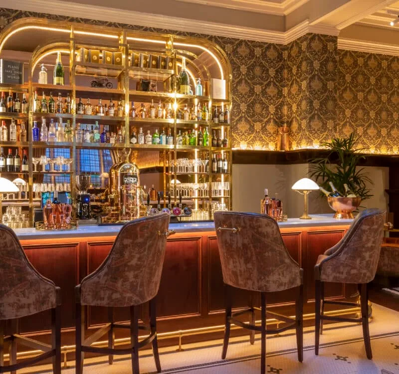 Hotel café-bar with velvet chairs and backlit shelves.