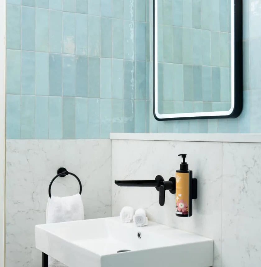Hotel bathroom with modern sink, illuminated mirror and blue tiles.