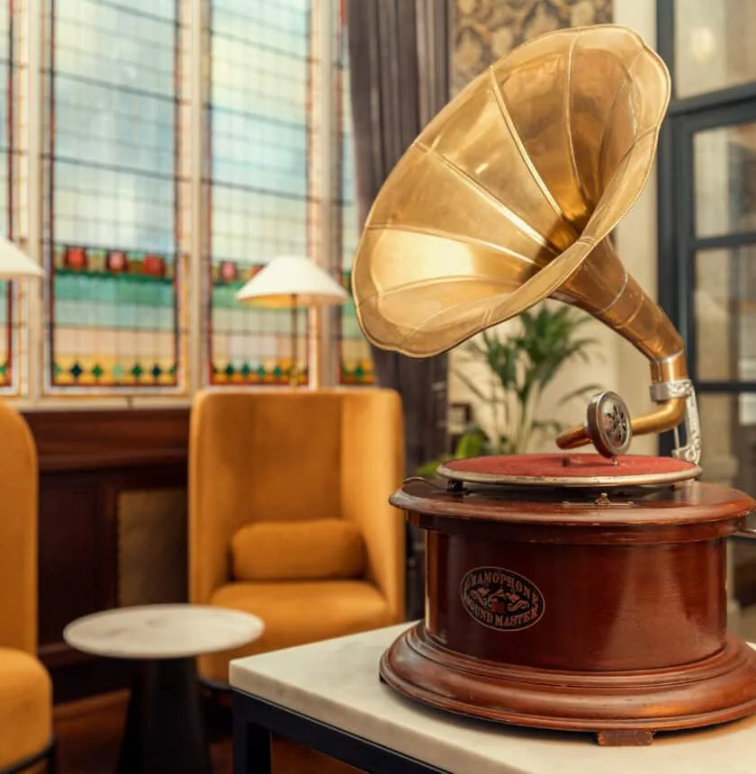 Hotel lounge with a gramophone, yellow armchairs and stained-glass windows.