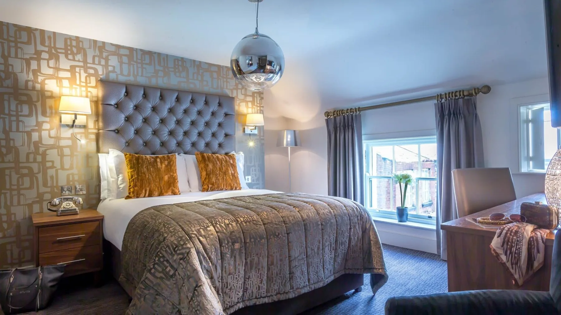 Hotel room with plush bedding, warm lighting and a large window.