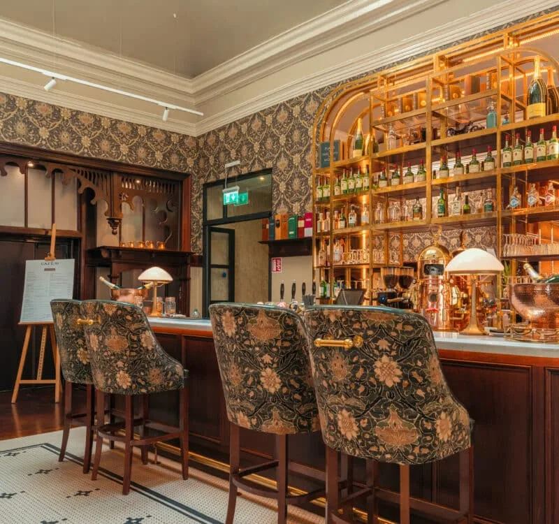 Hotel bar with leather chairs, warm lighting and shelves.