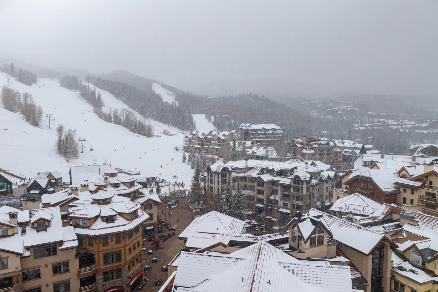 A snowy mountain resort village sits beneath ski slopes on an overcast day.