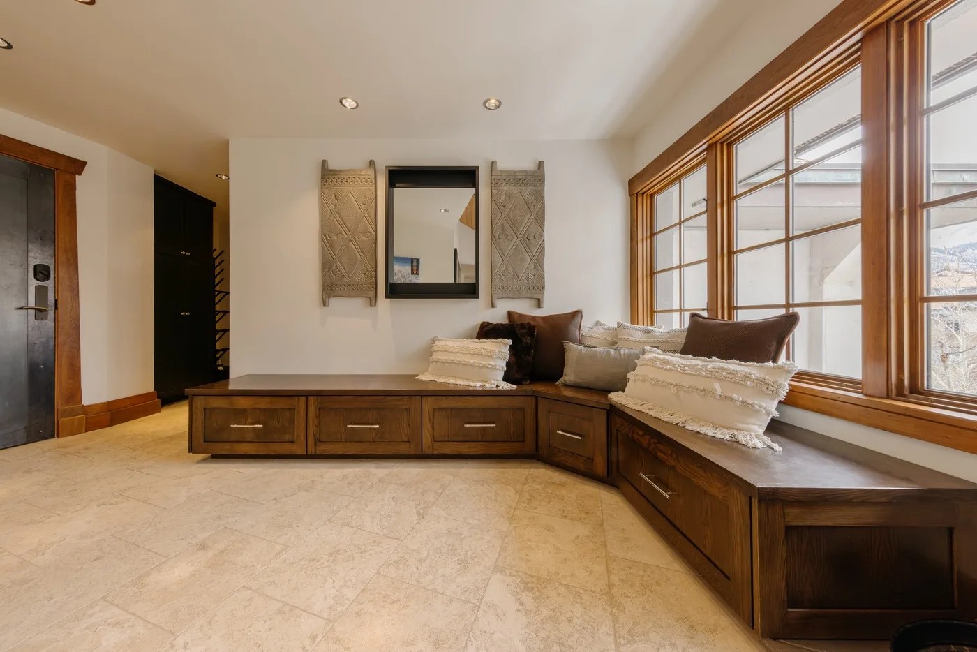 A bright sitting area features built-in wooden seating beneath large windows.