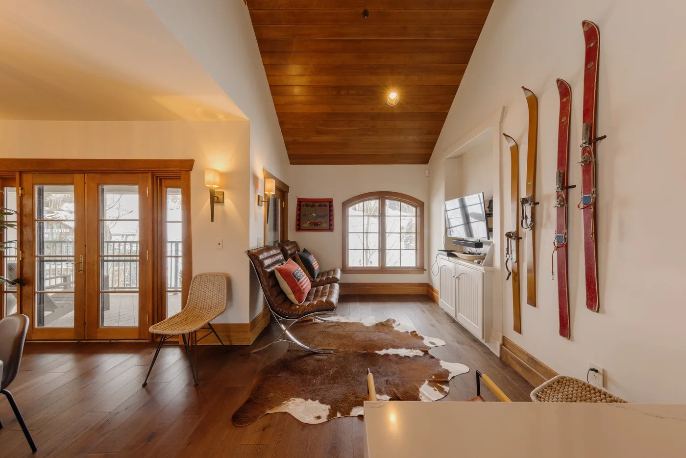 A bright living room with a wood ceiling, large windows, and a television.