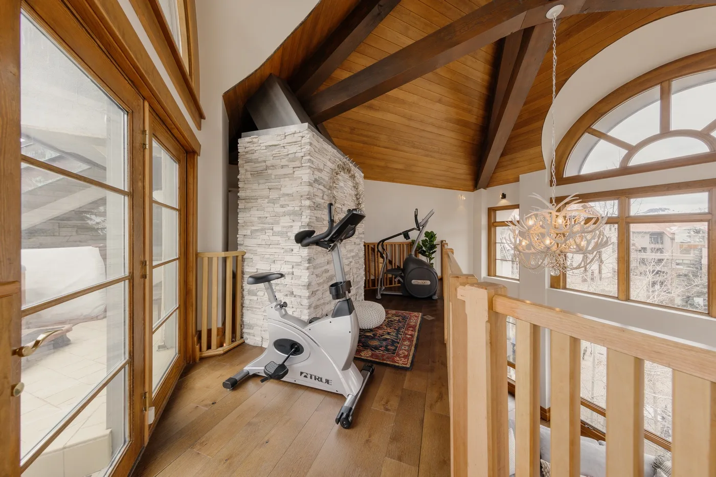 A home gym occupies a loft with a stone fireplace and exercise equipment.