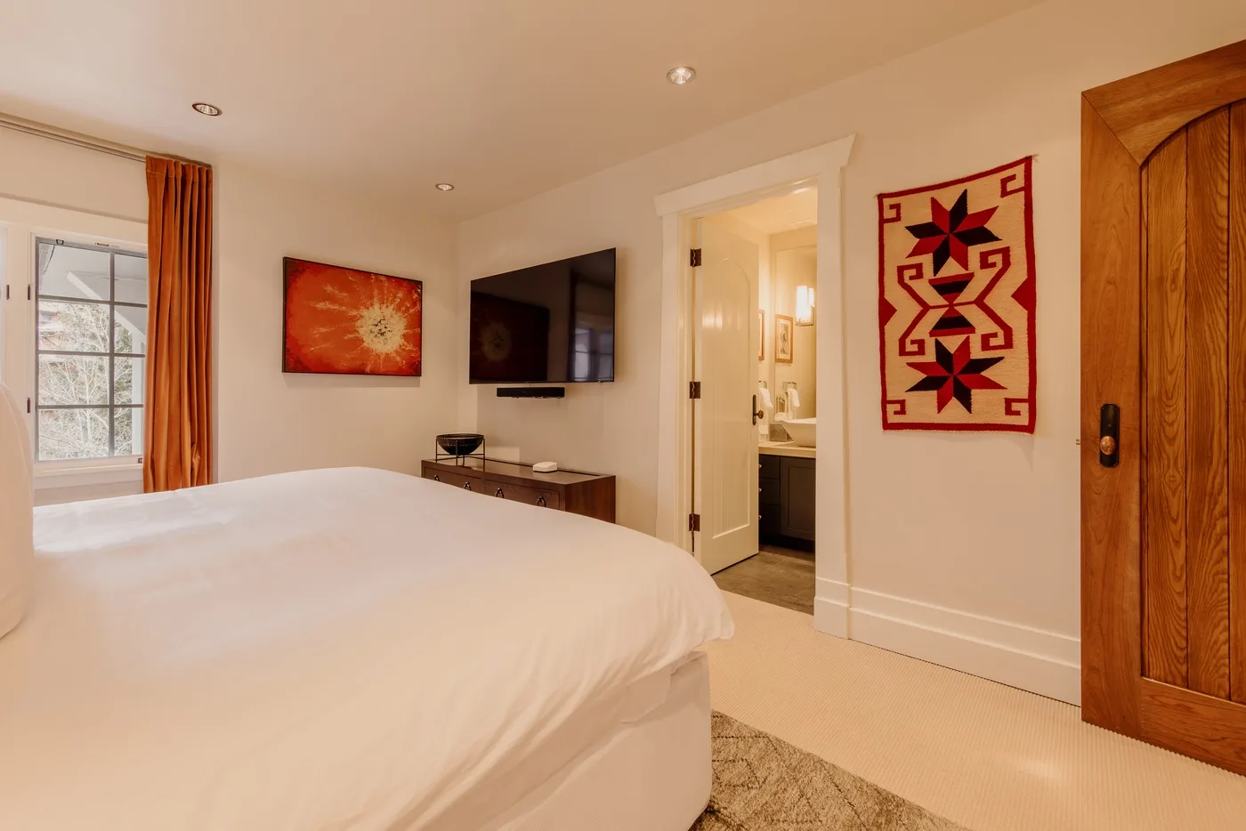 A bedroom with a large bed, a wall-mounted television, and an open bathroom doorway.