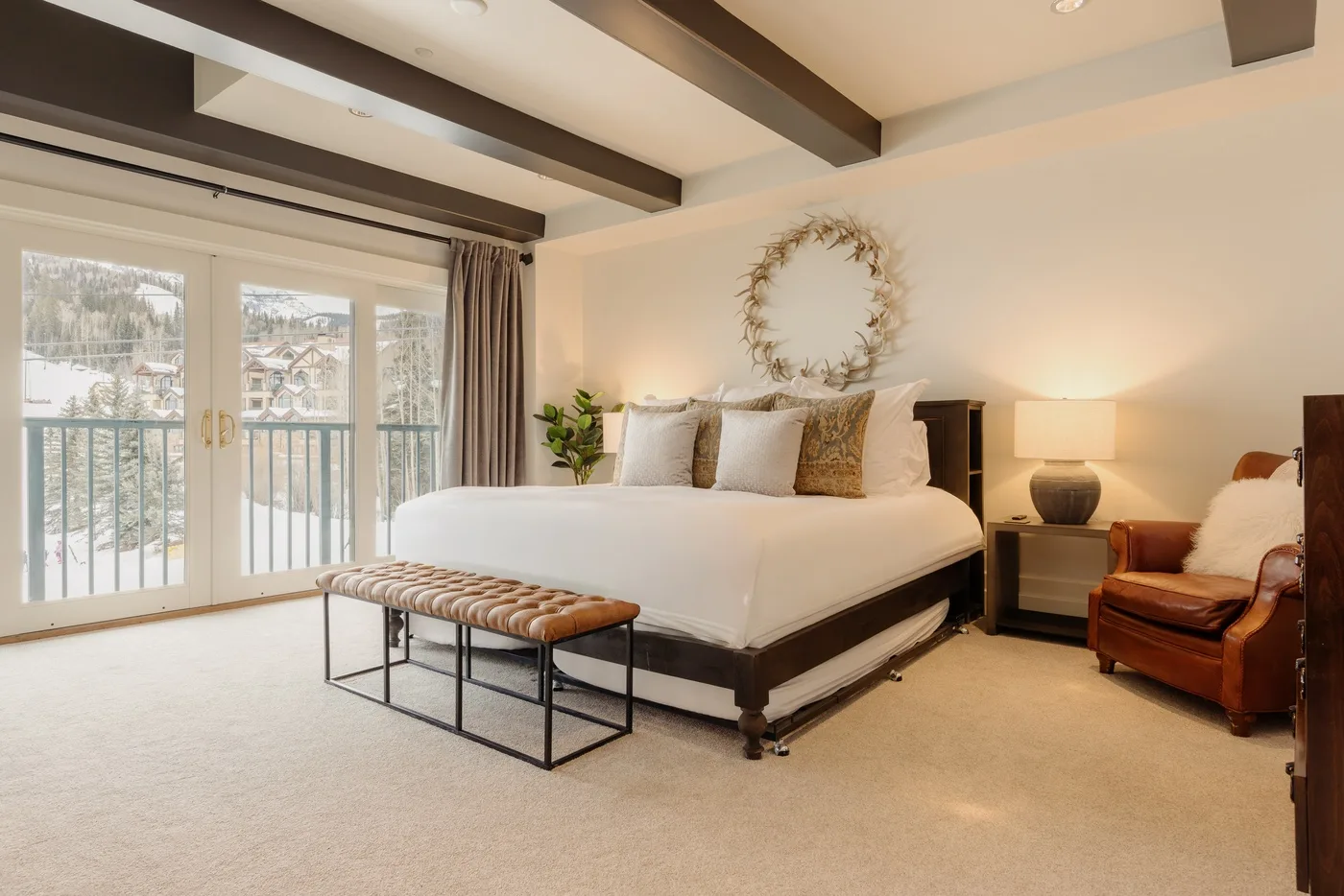 A bedroom with a large bed, a cushioned bench, and windows opening onto a balcony.