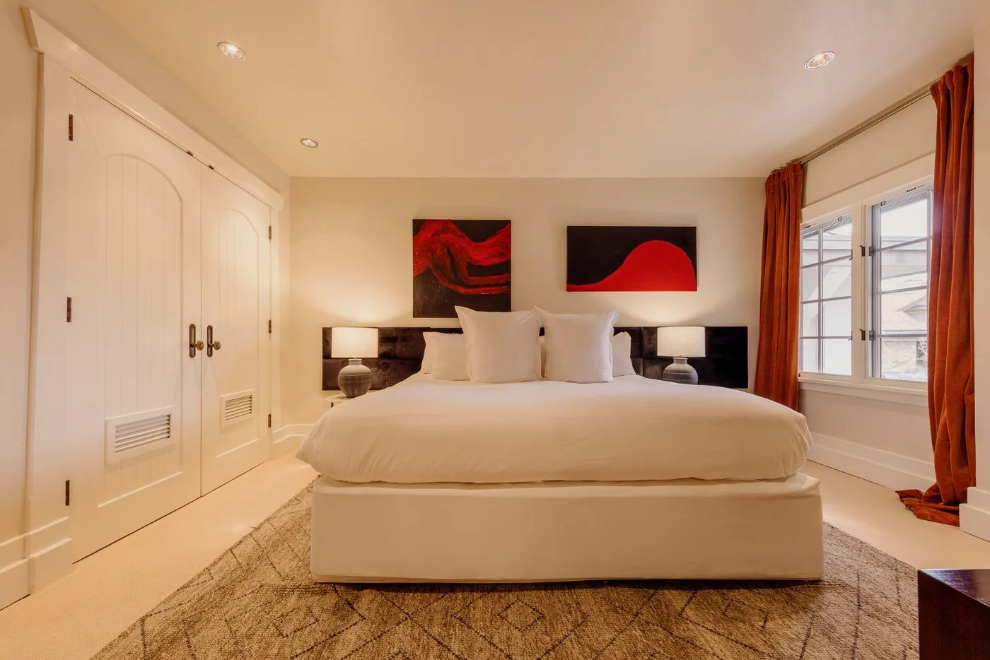 A bedroom with a large bed, bedside lamps, and windows framed by curtains.
