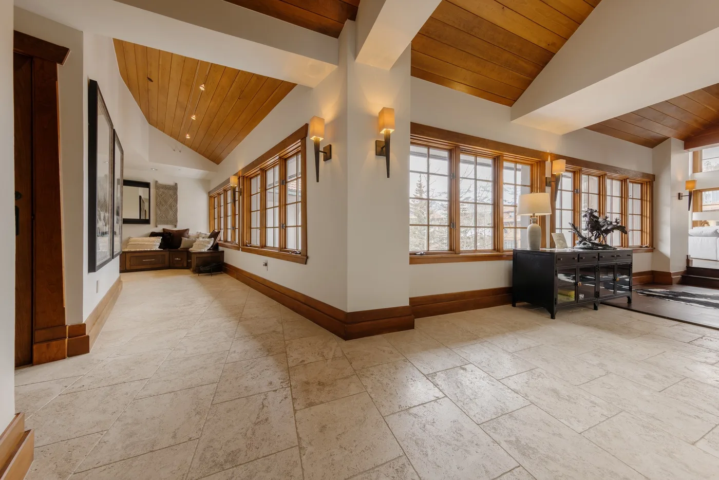 A bright open living area has large windows and a sloped wood ceiling.