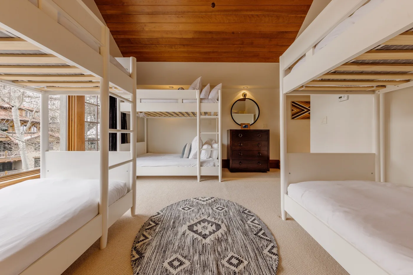 A bedroom with bunk beds, a wooden ceiling, and a patterned rug.