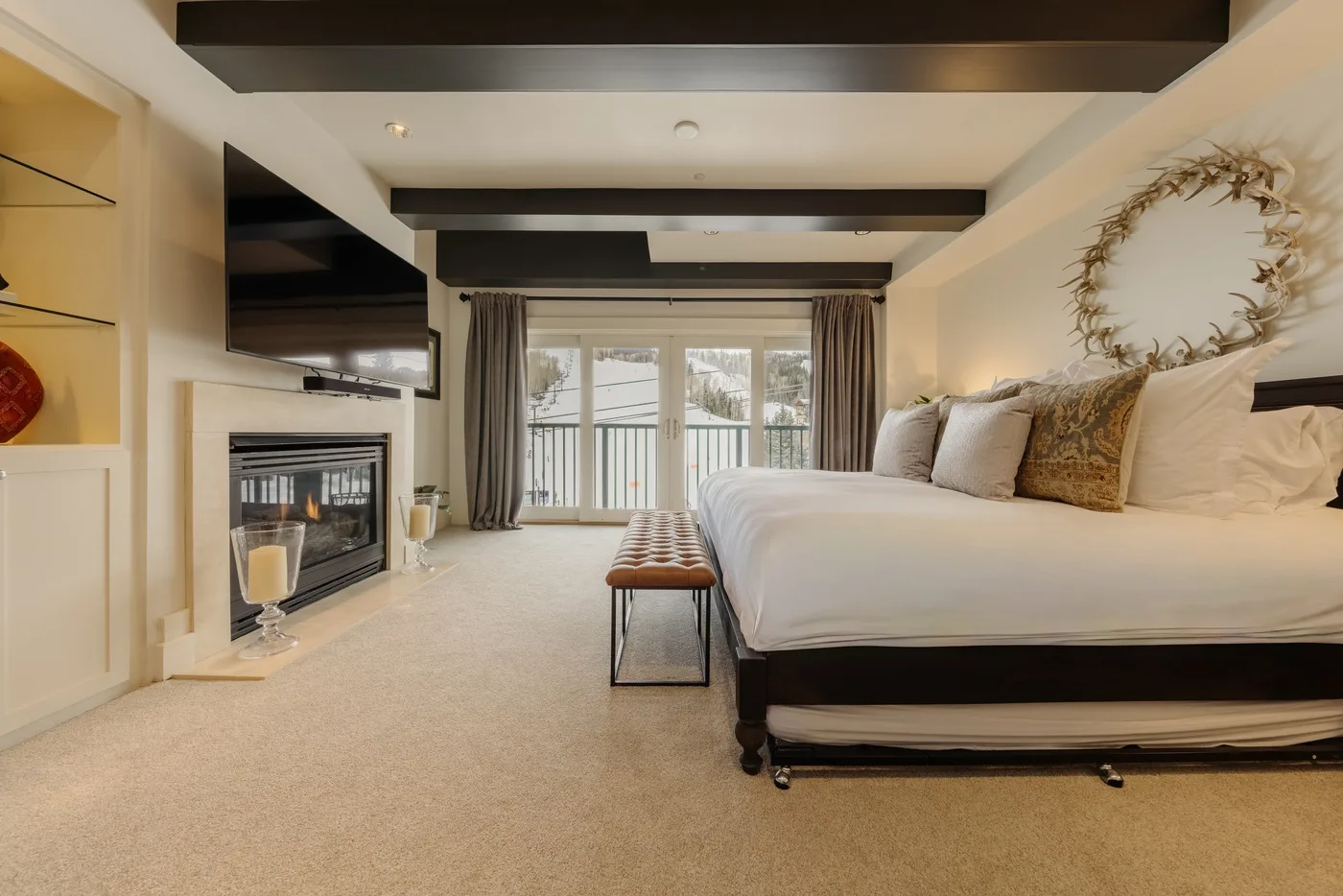 A bedroom with a large bed, a bench, and glass doors opening to a balcony.