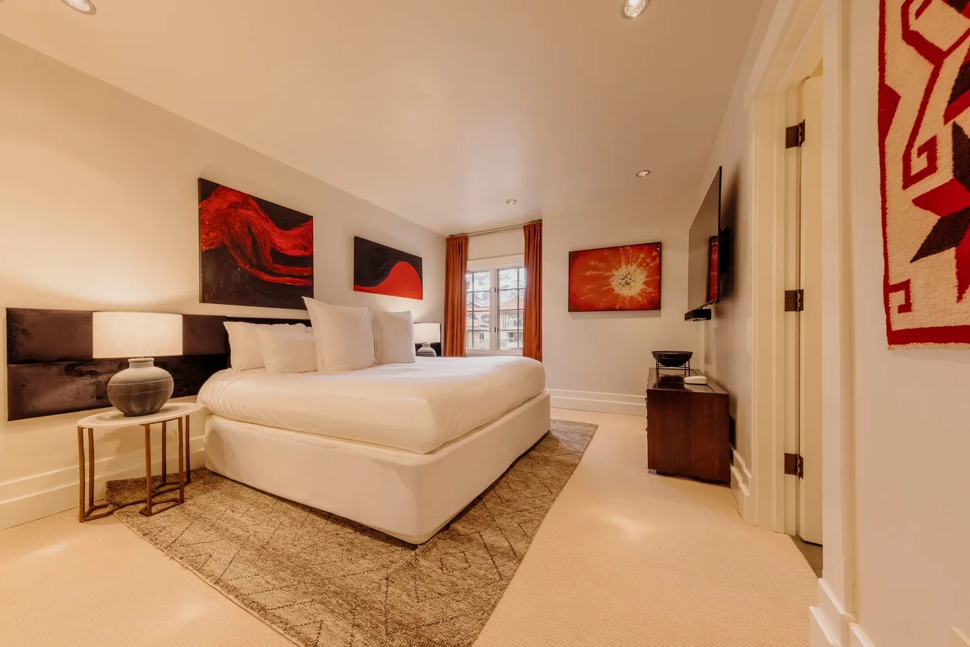 A bedroom with a large bed, artwork, and a window with curtains.