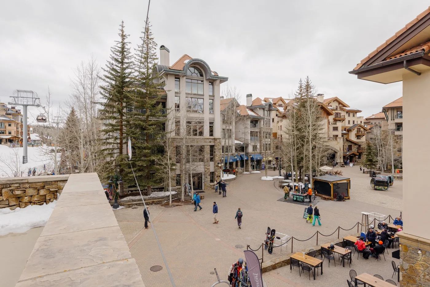 A pedestrian plaza between alpine-style buildings, with outdoor seating and patches of snow.