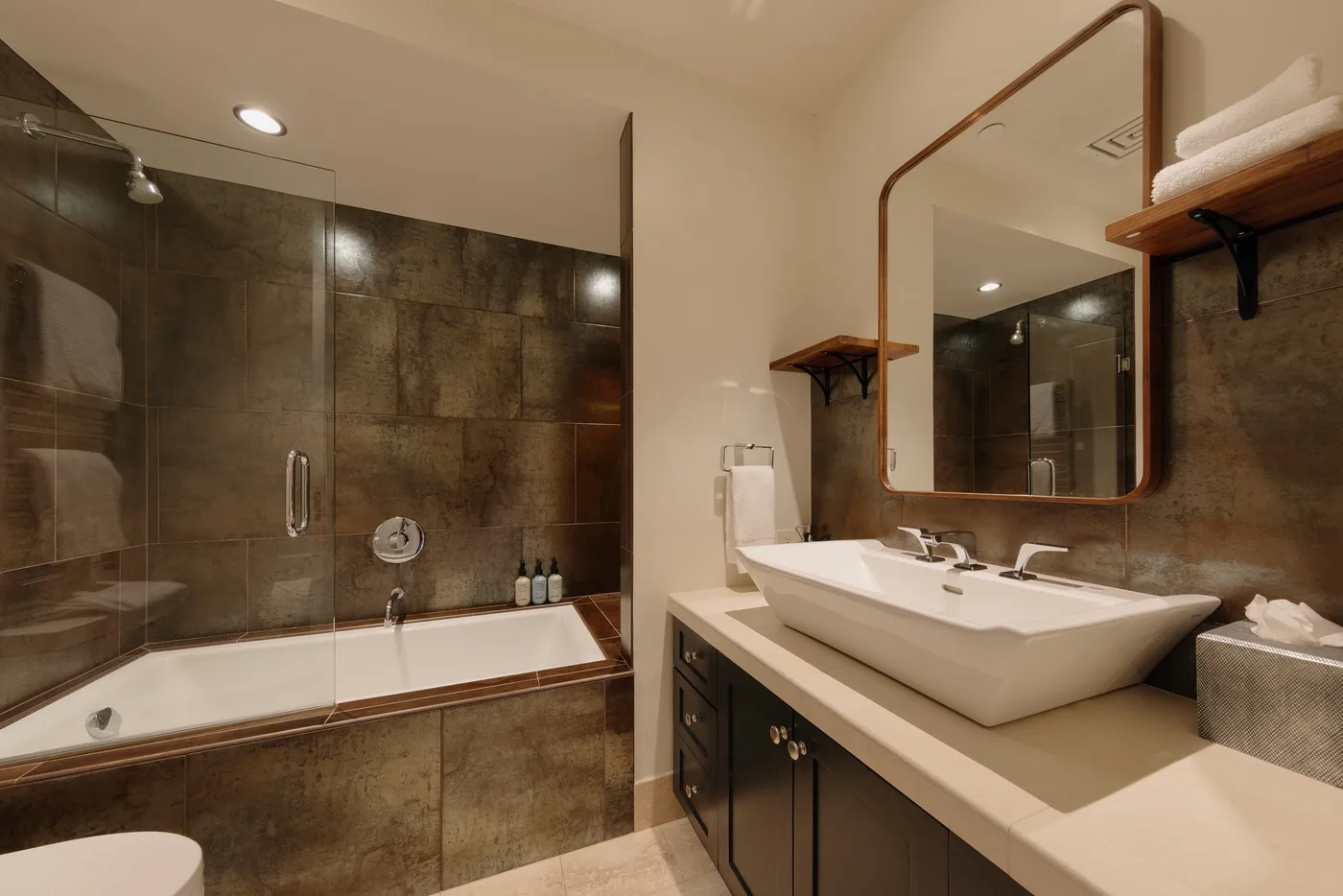 A bathroom with a bathtub, glass shower screen, and sink vanity.