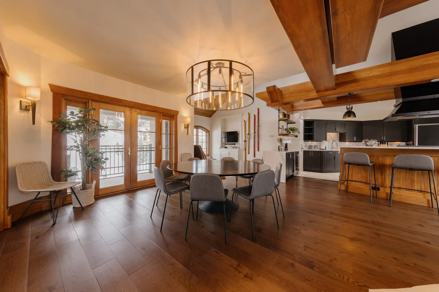 An open dining and kitchen area features a table, seating, and wooden ceiling beams.