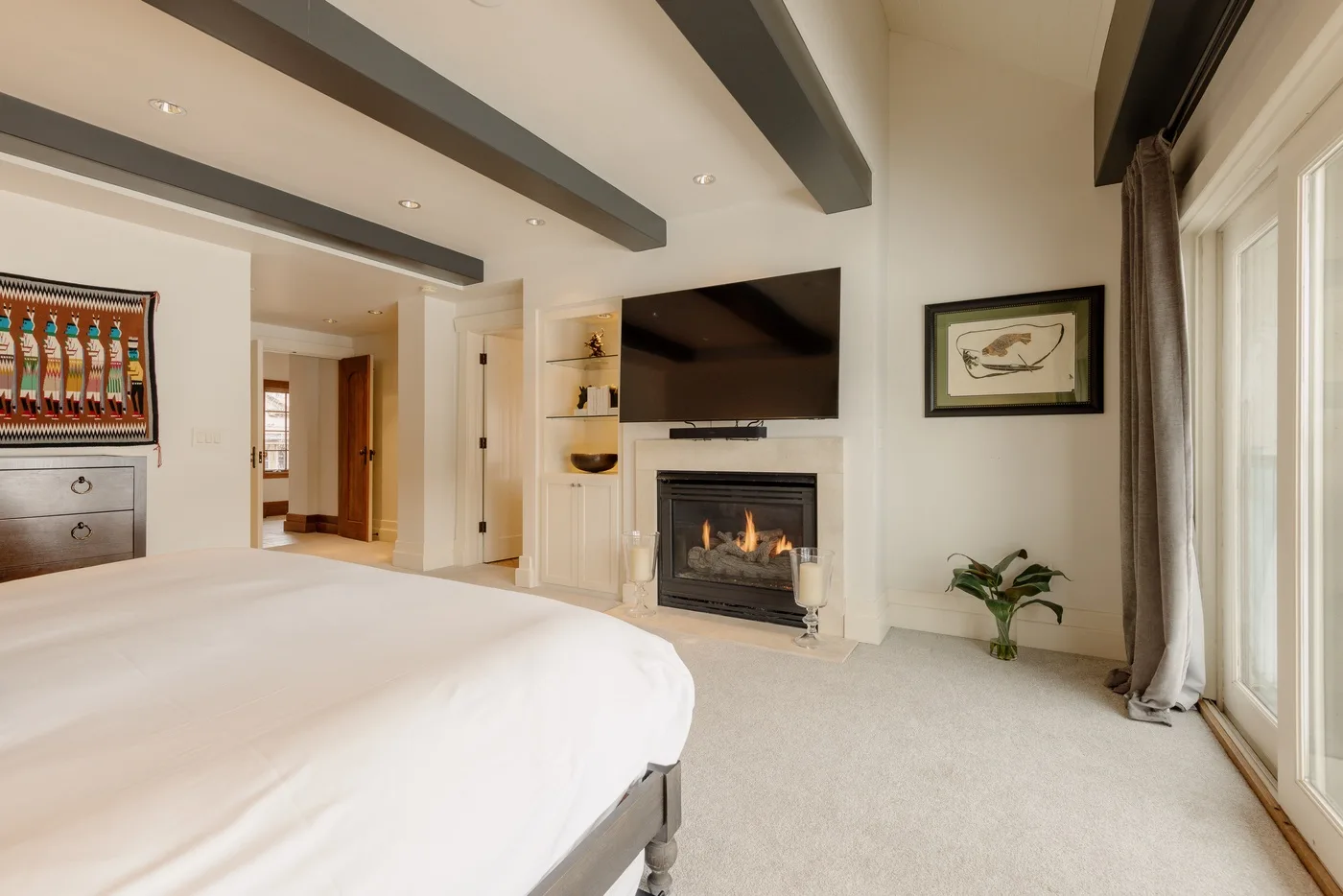 A bedroom with a large bed, a fireplace, and a wall-mounted television.