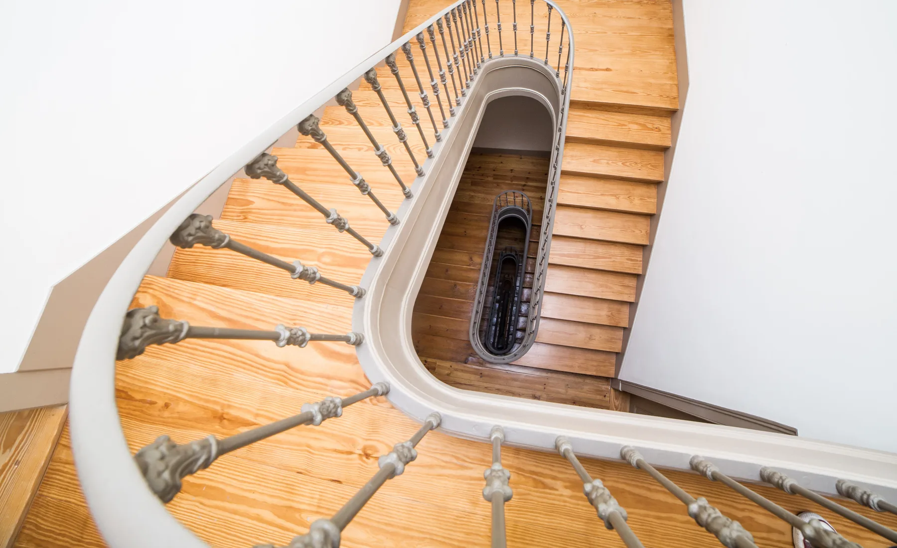 Una escalera curva con peldaños de madera y una barandilla metálica.
