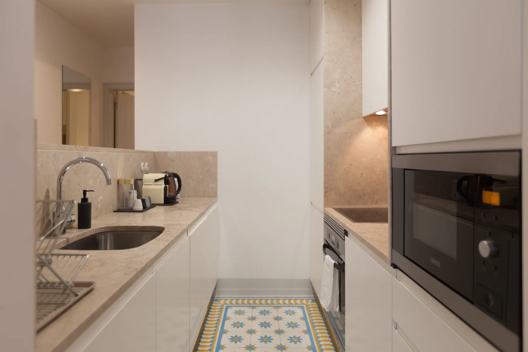 Una cocina estrecha tiene encimeras claras, un fregadero y electrodomésticos empotrados.