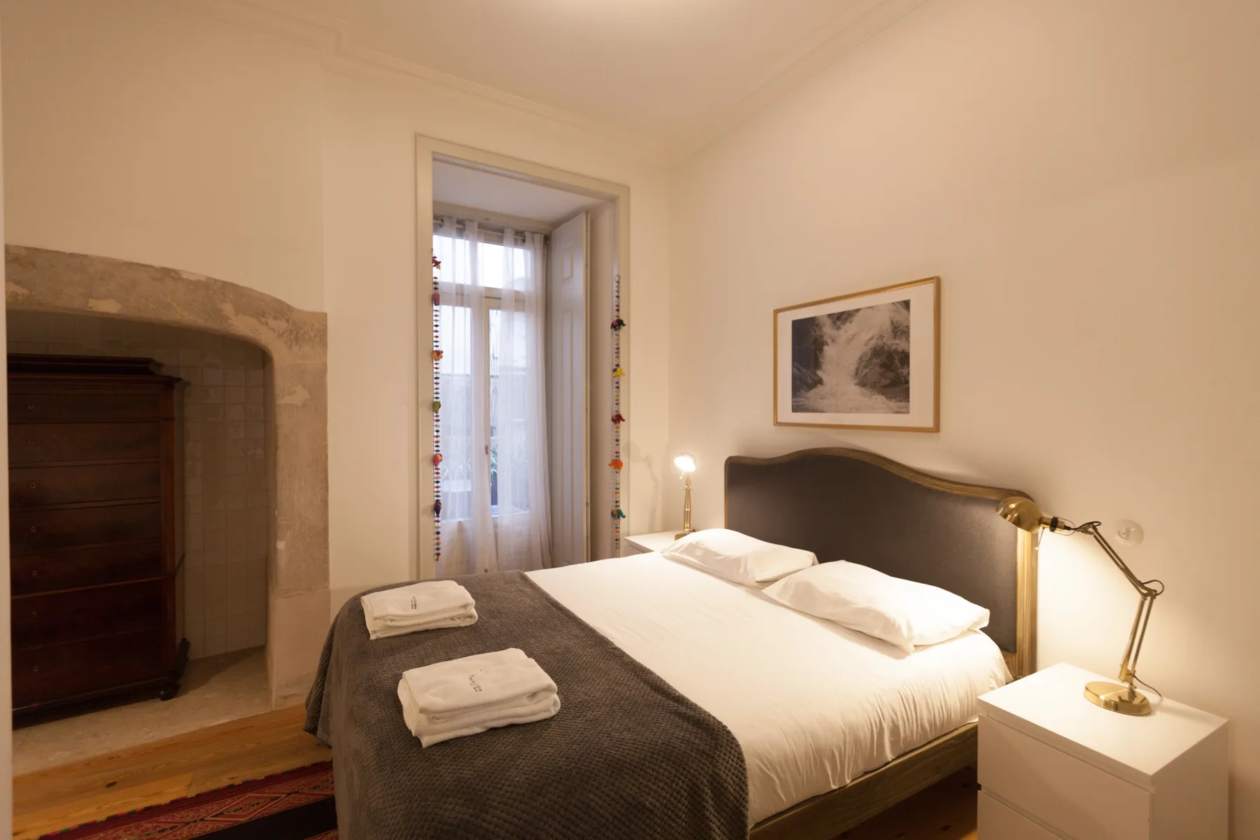 Dormitorio con una cama bien tendida y una ventana con cortinas translúcidas.