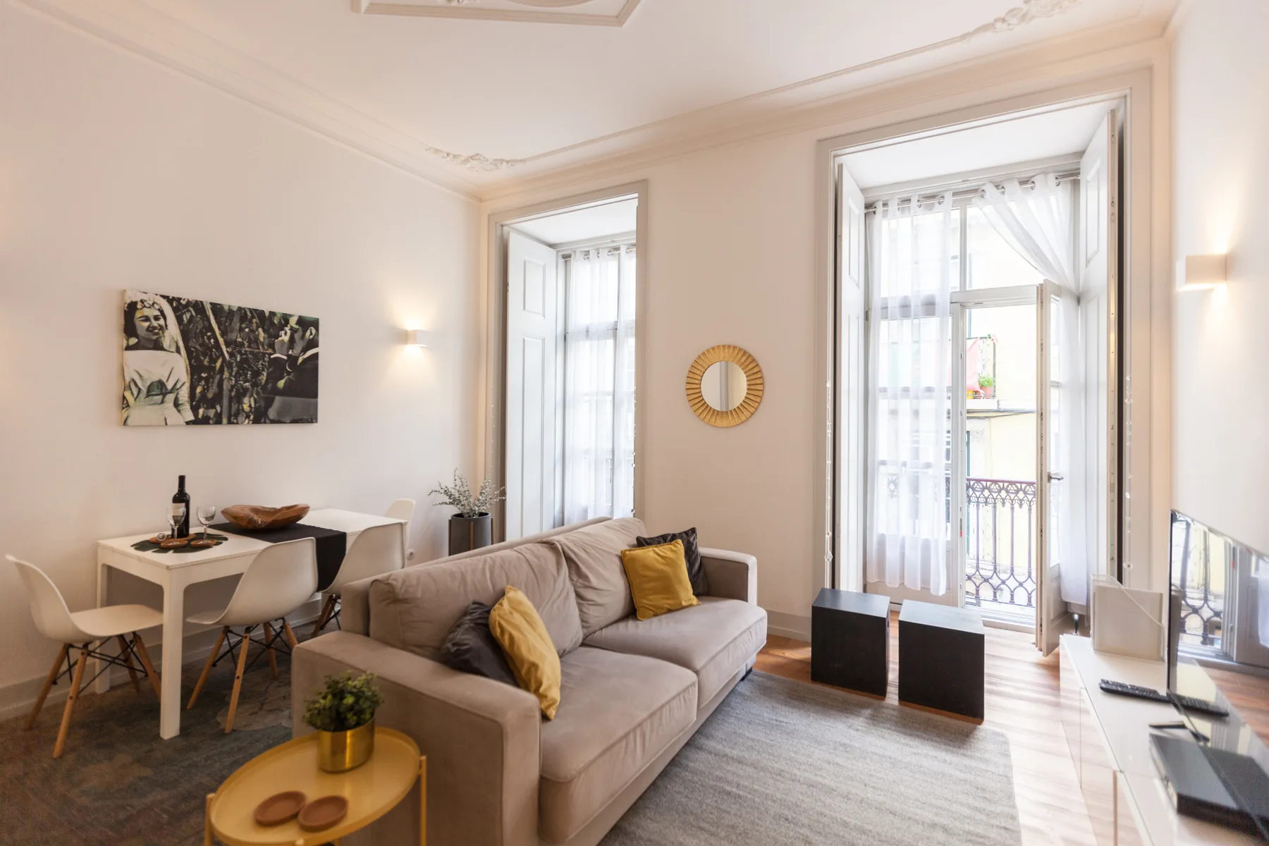 Un salón luminoso con asientos, una mesa de comedor y ventanas altas que dan a un balcón.