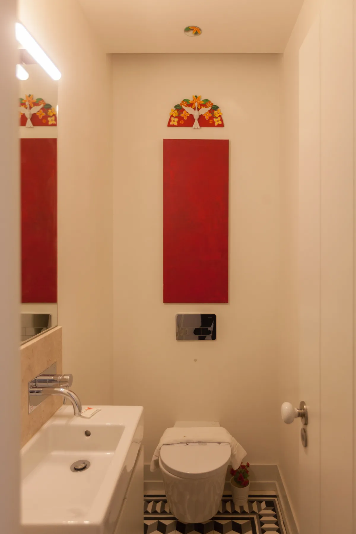Un baño con lavabo, inodoro y un panel rojo en la pared.