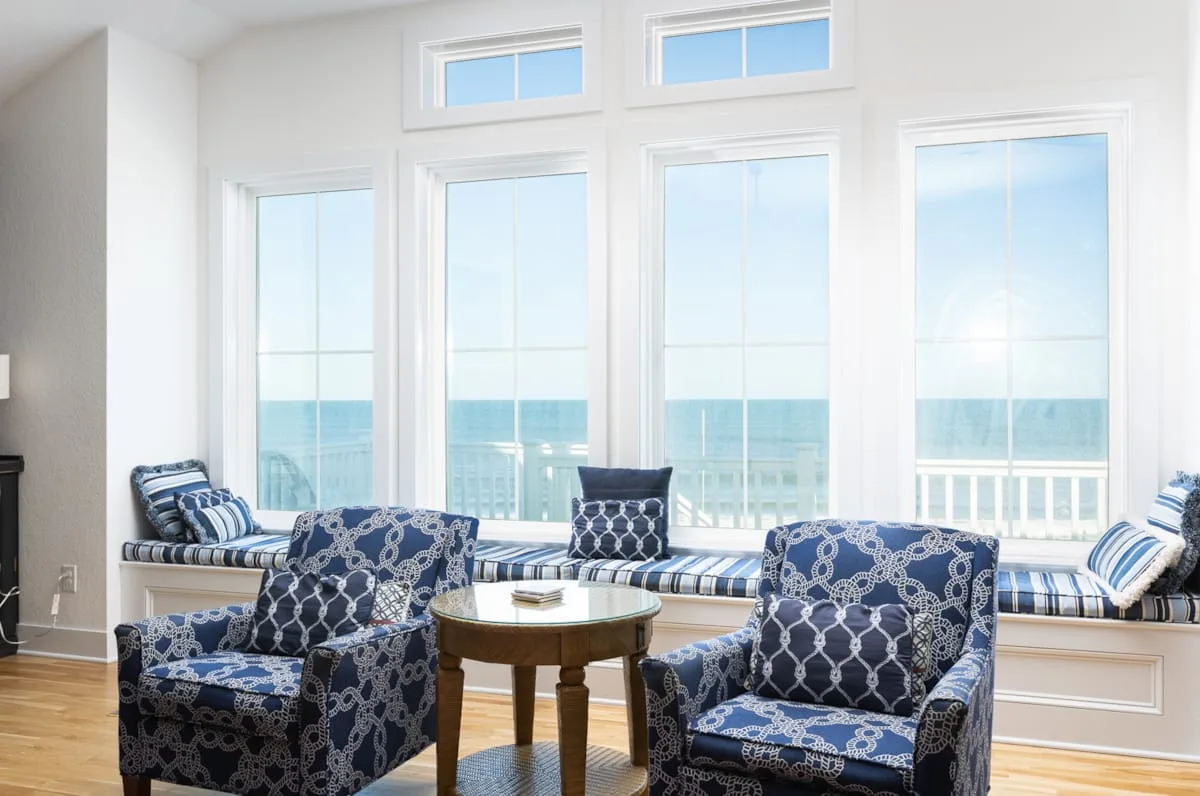 Una sala luminosa con asientos estampados y grandes ventanas con vistas al agua.