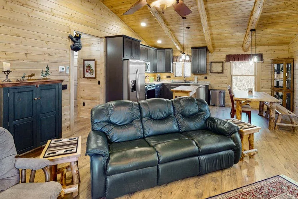 A wood-paneled living and dining area with a dark sofa and kitchen in the background.