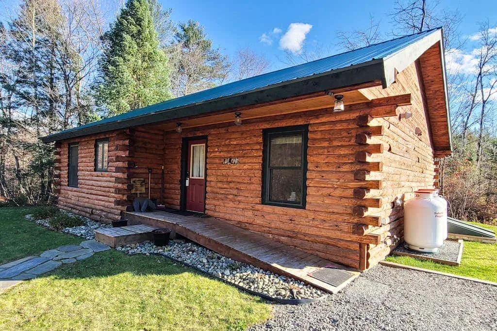 A log cabin exterior with a red door and dark-framed windows.