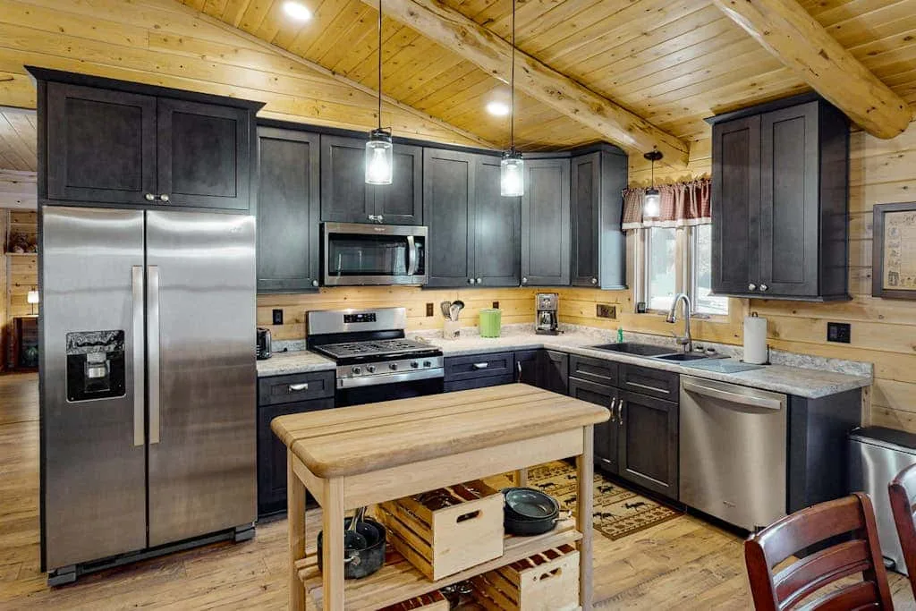 Una cocina con gabinetes oscuros, electrodomésticos de acero inoxidable y una isla de madera.