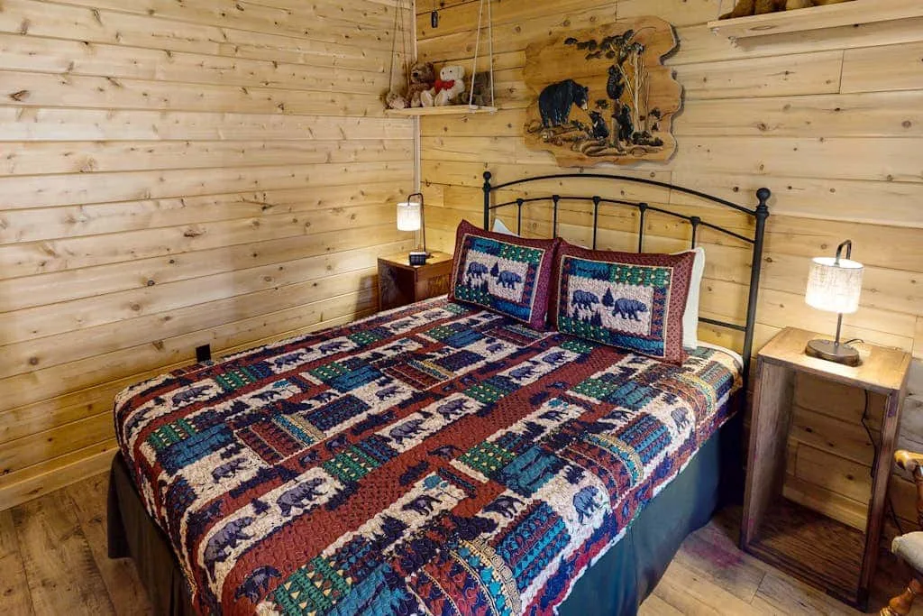 Un dormitorio con una cama cubierta por una colcha colorida y paredes de madera.