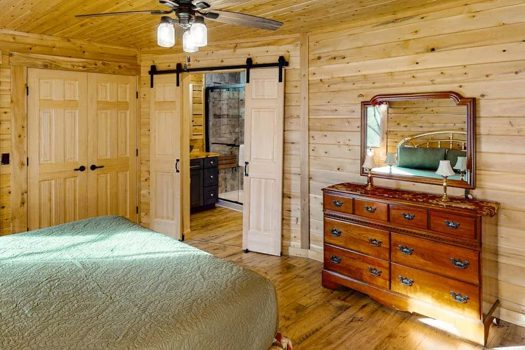 Dormitorio revestido de madera con cama, cómoda y puerta abierta.