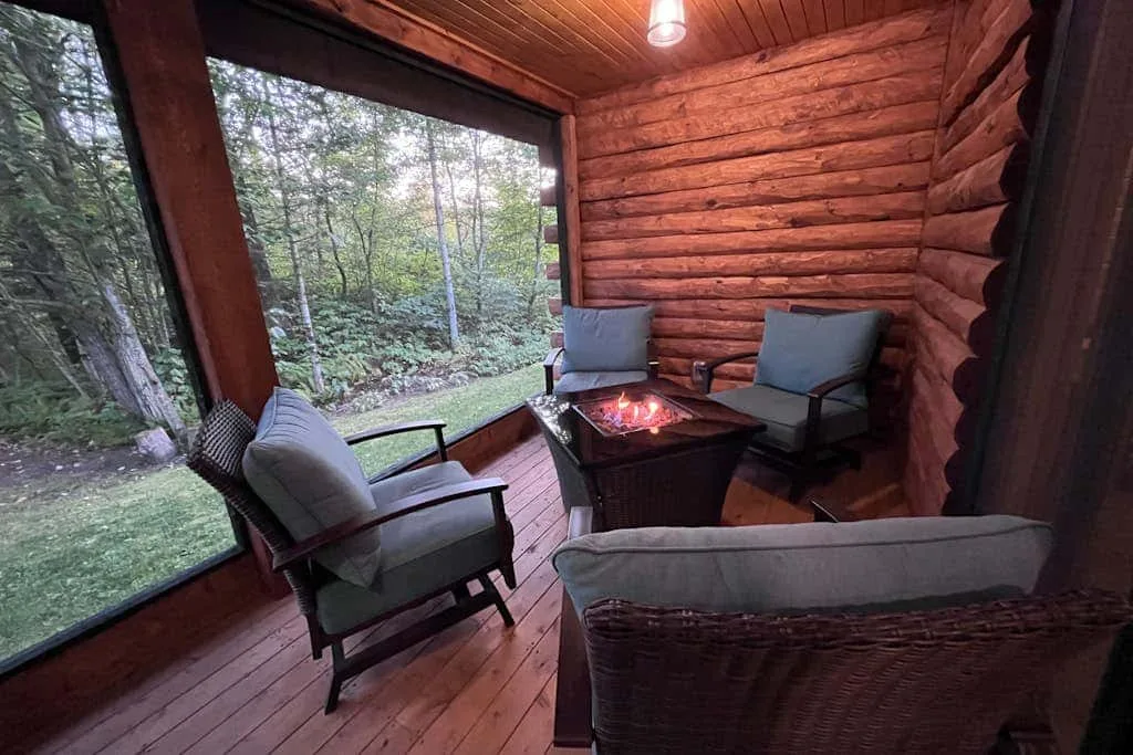 Una zona de estar con paredes de madera, asientos acolchados y una pequeña mesa de fuego junto a una ventana grande.