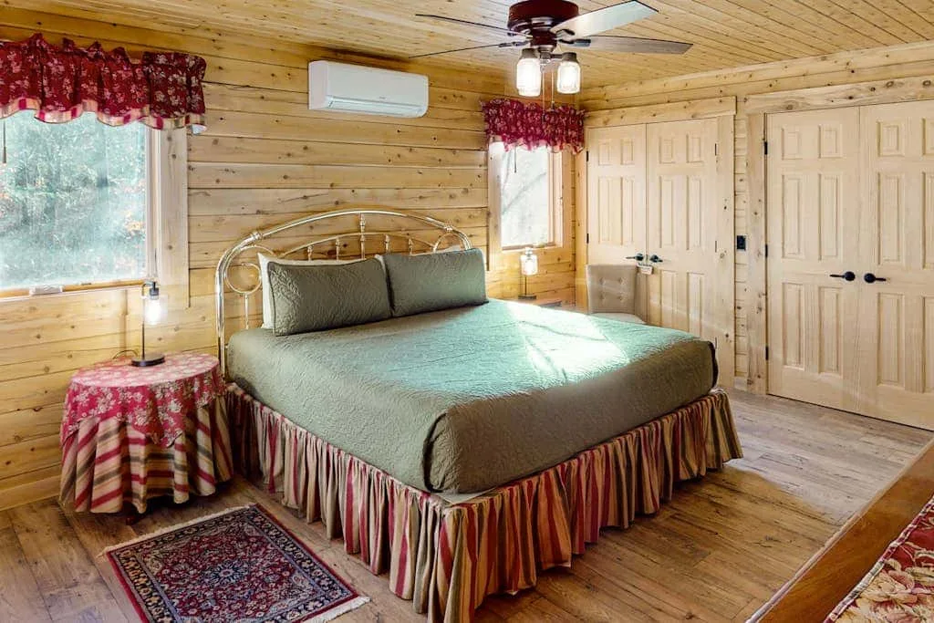 Un dormitorio con una cama grande, paredes de madera y ventanas con cortinas estampadas.