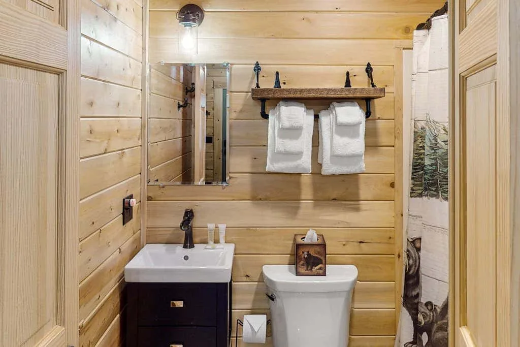Un baño con paredes de madera, lavabo, inodoro y toallas colgadas en la pared.