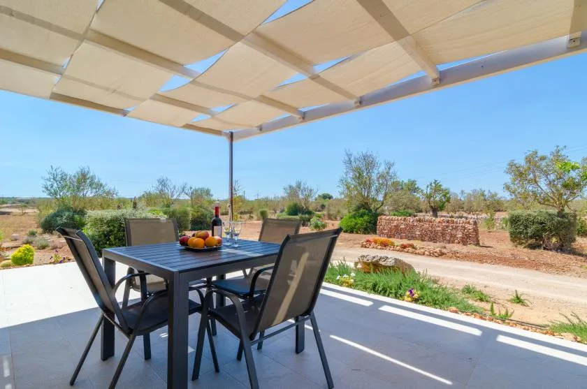 Un patio cubierto con mesa y sillas da a un jardín ajardinado.