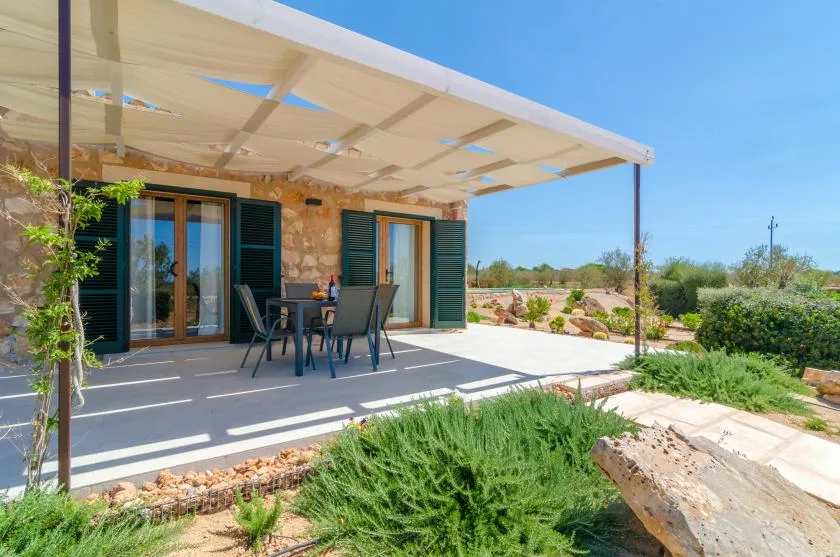 Un patio exterior sombreado con una mesa de comedor junto a un edificio revestido de piedra.
